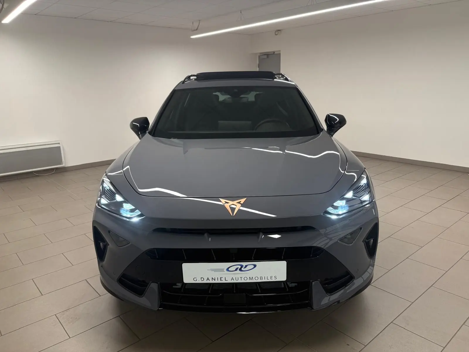 Vue frontale d'un CUPRA Formentor 2025 gris graphène avec phares allumés et toit ouvrant panoramique visible.