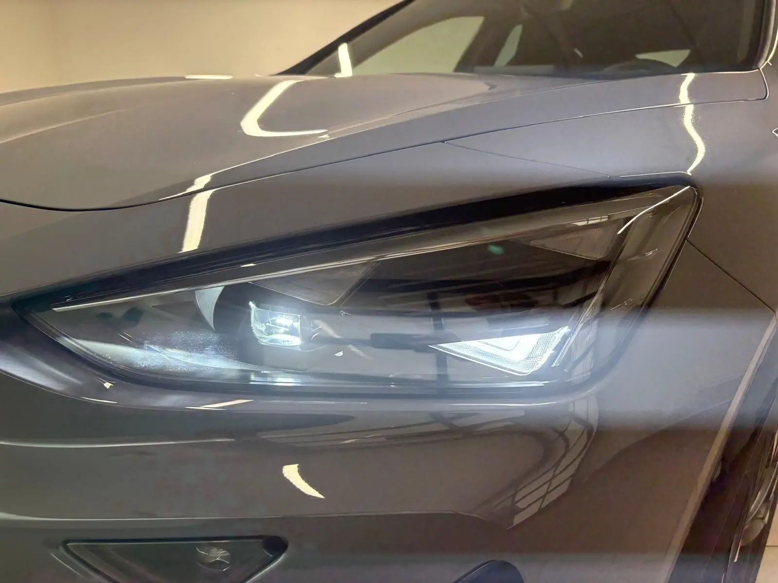 Gros plan sur le phare avant droit du CUPRA Formentor 2025 gris graphène avec peinture spéciale et toit ouvrant panoramique visible.