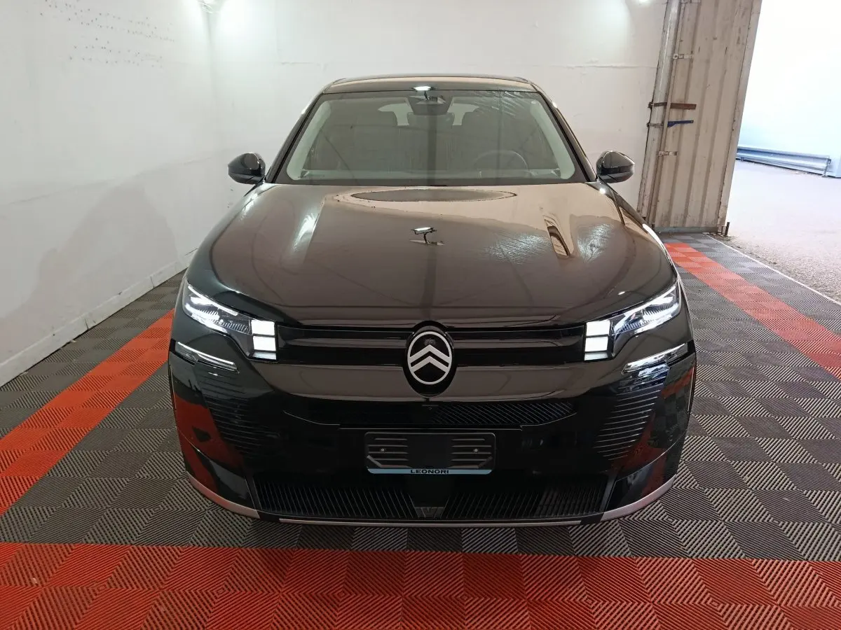 Citroën C5 Hybride noir vue de face dans un garage, avec phares LED allumés et logo distinctif au centre.