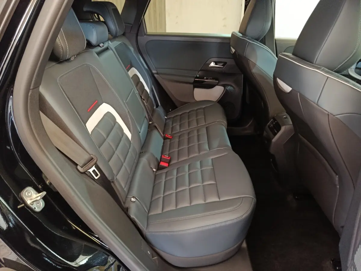 Vue intérieure côté gauche des sièges arrière noirs en cuir du Citroën C5 Hybride 2026 avec surpiqûres blanches et ceintures rouges.