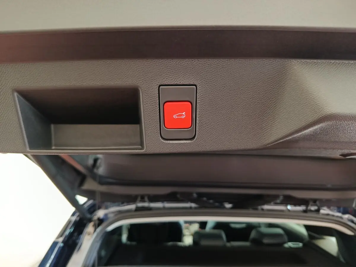 Bouton rouge d'ouverture électrique du coffre sur la trappe arrière d'une Citroën C5 Hybride noire, vue intérieure du coffre ouvert.