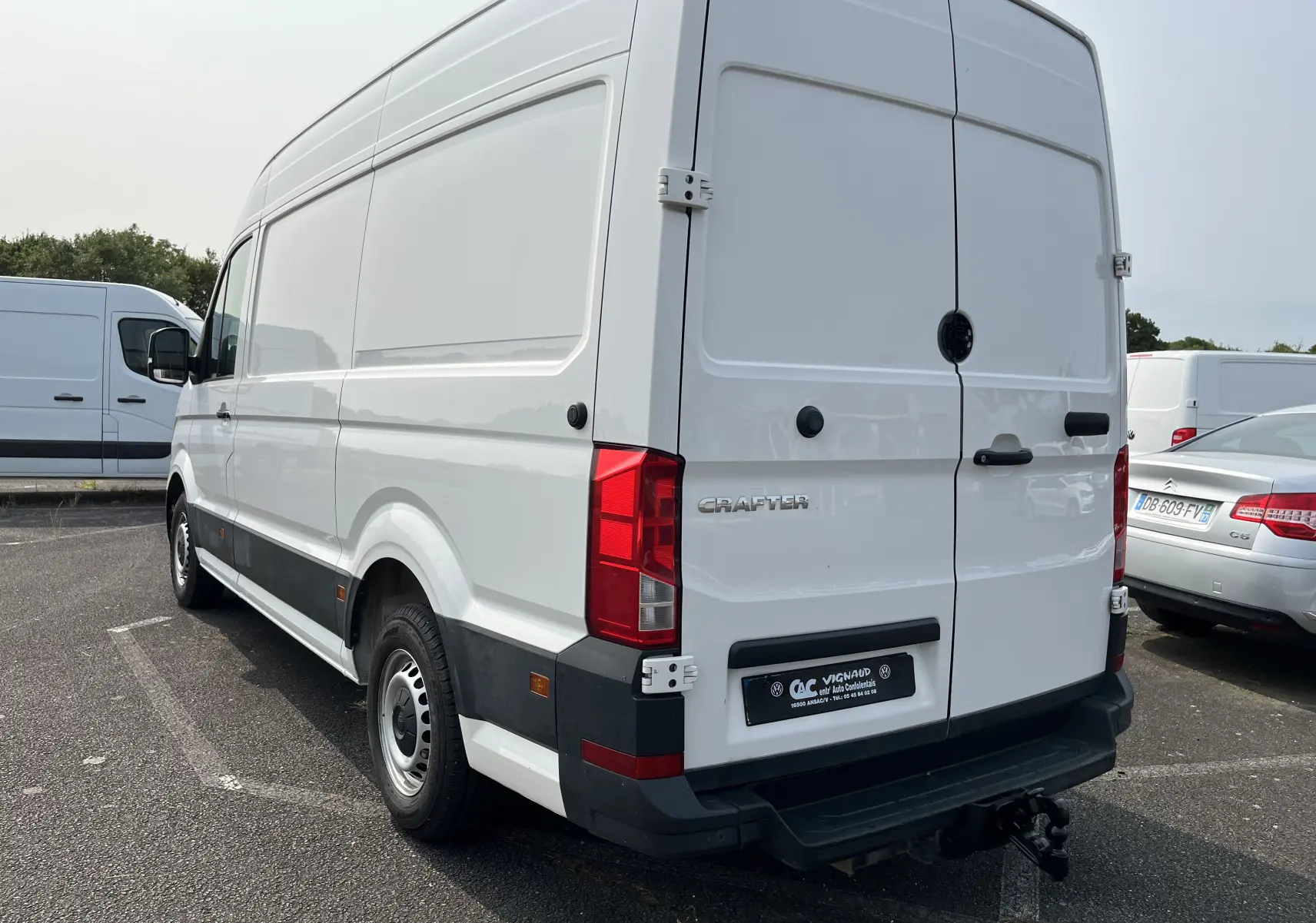 Vue 3/4 arrière droite d'un Volkswagen Crafter blanc fourgon avec hayon et attelage de remorque visible.