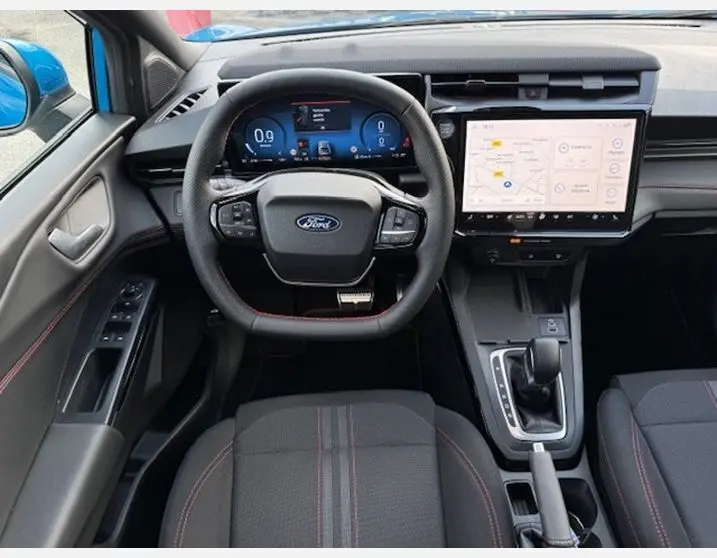 Vue intérieure avant du Ford Puma bleu Aqua Blue 2025, tableau de bord numérique et écran tactile central avec sièges sport surpiqués rouges.