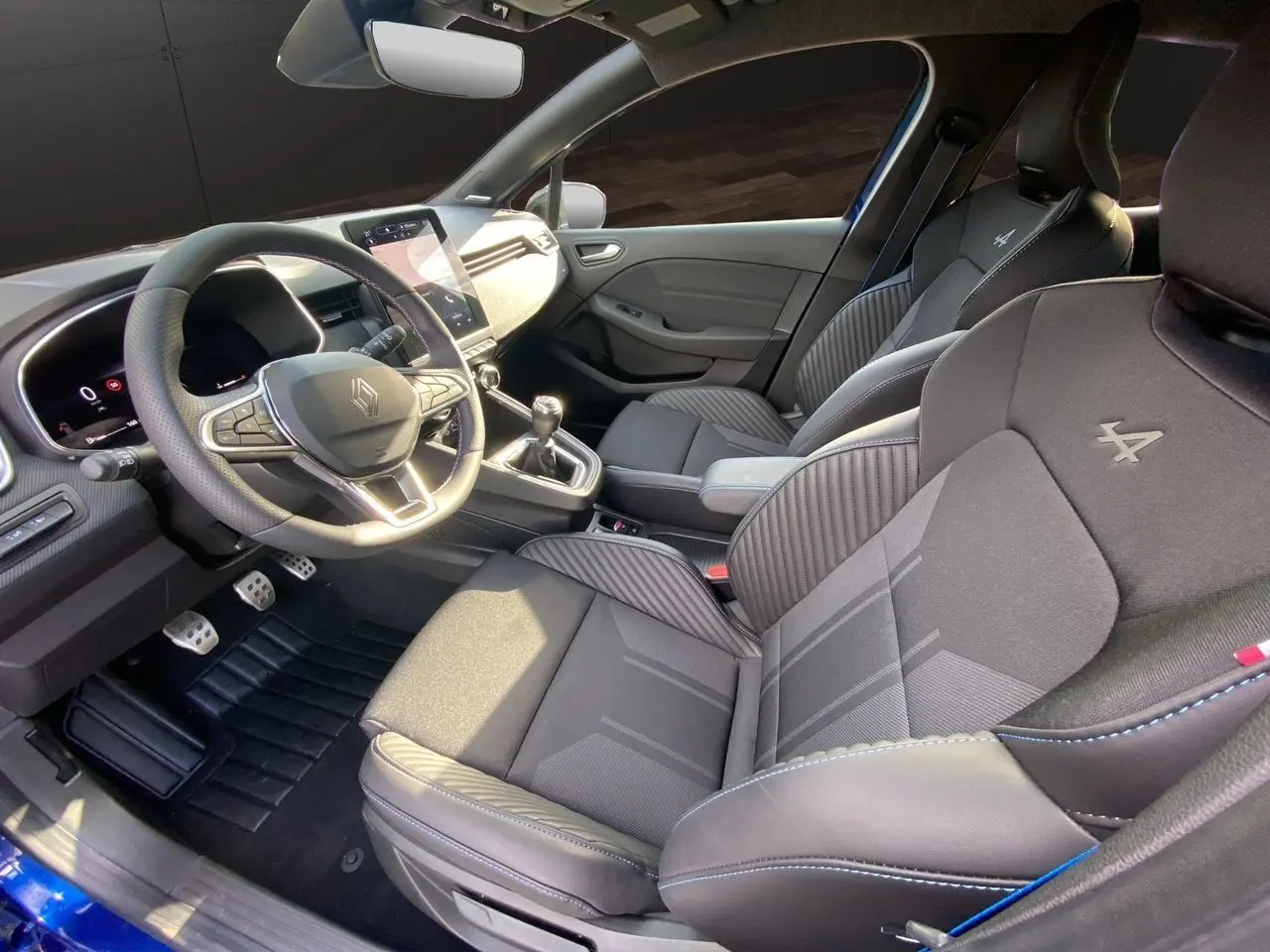 Intérieur noir de la Renault Clio V TCE 90 Esprit Alpine, vue côté conducteur avec sièges sport et volant multifonction.