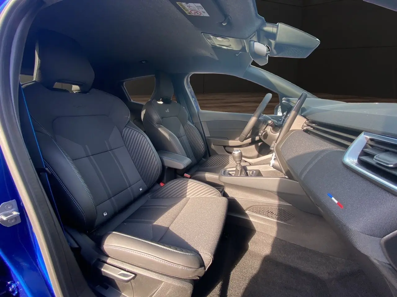 Intérieur noir de la Renault Clio V TCE 90 Esprit Alpine, vue côté conducteur avec volant et console manuelle visibles.