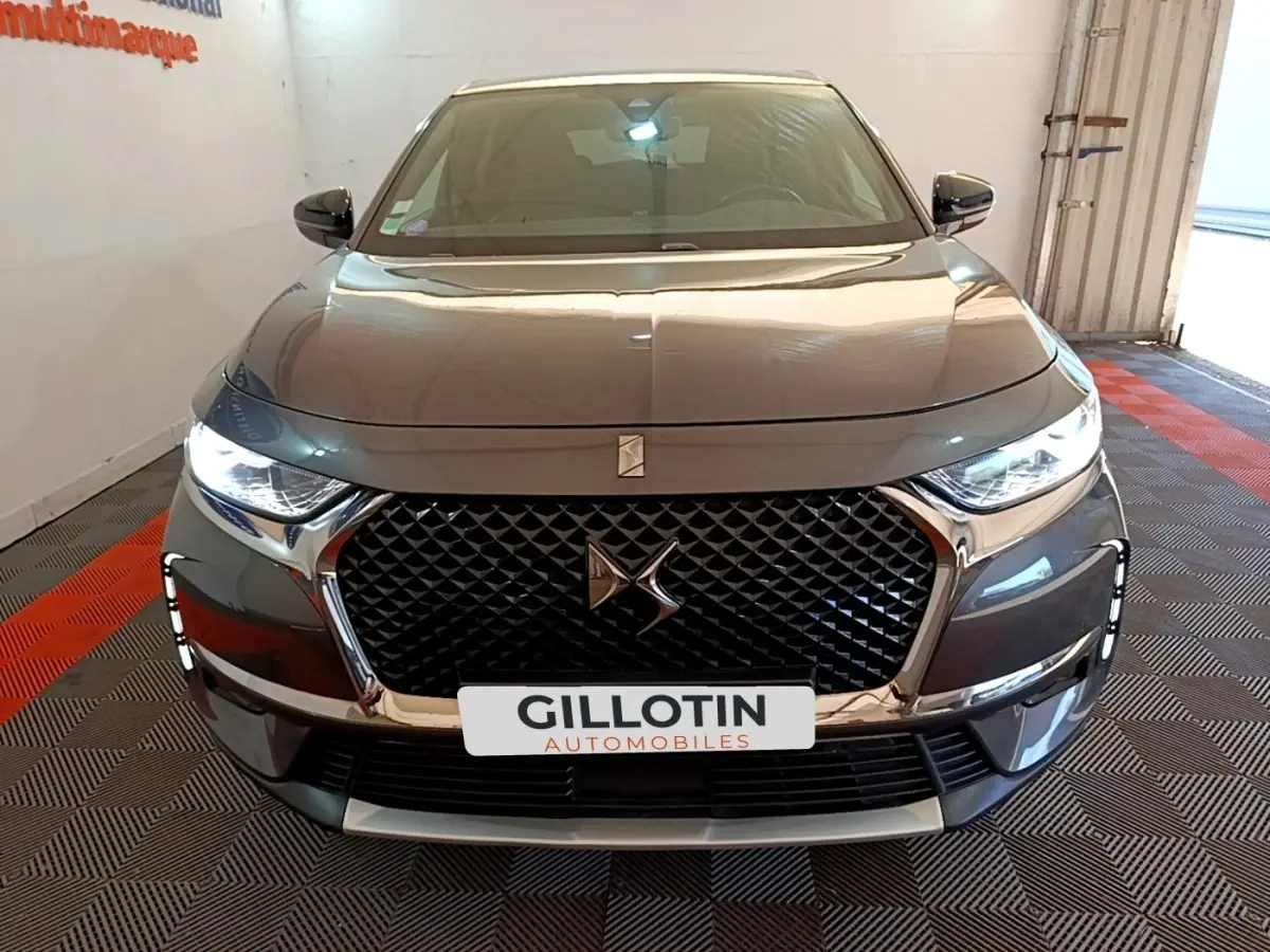 Vue avant d'un DS7 Crossback gris foncé avec calandre distinctive et phares LED allumés en intérieur.