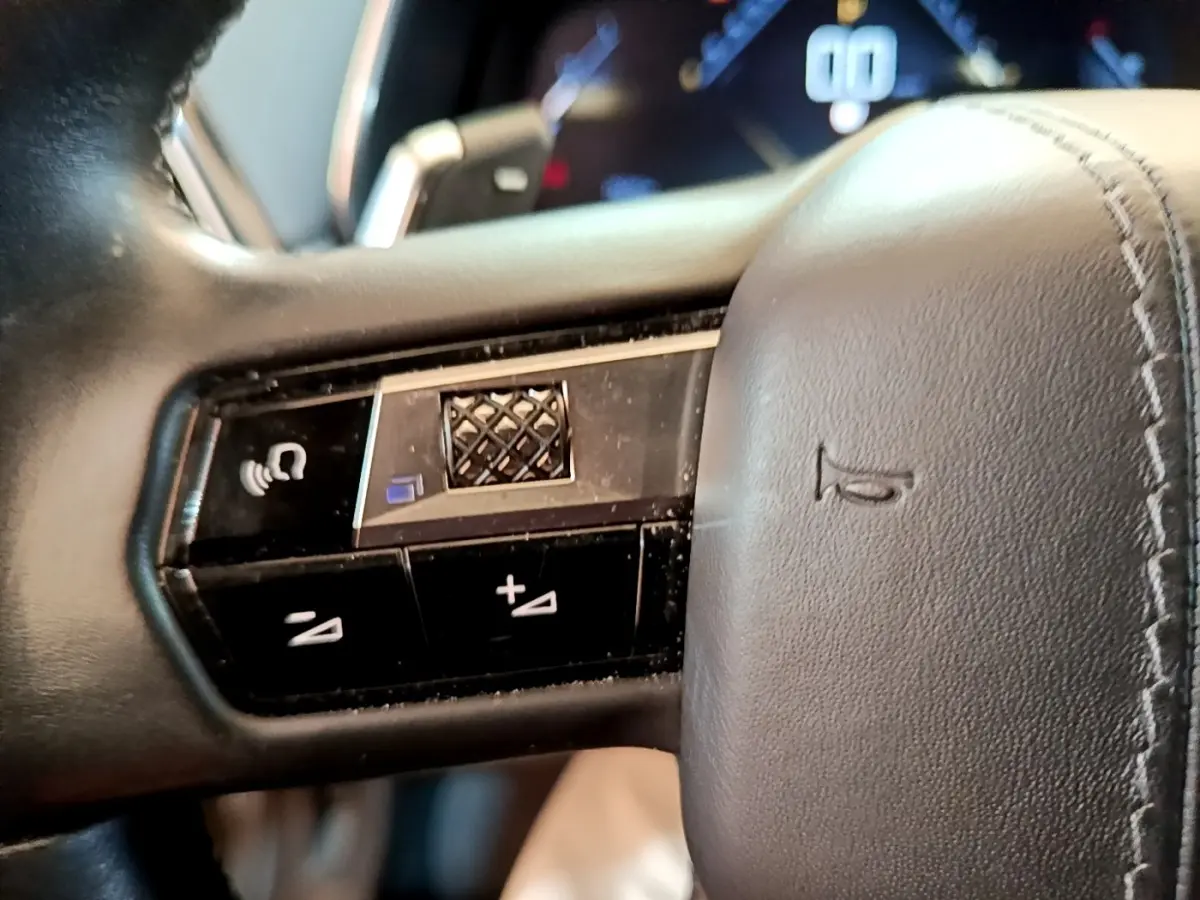 Gros plan sur les commandes du volant en cuir noir du DS7 Crossback PureTech 180, affichage digital en arrière-plan flou.