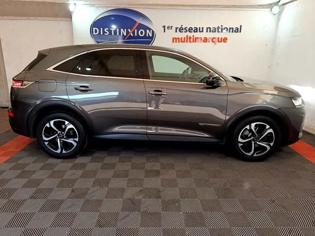 Vue latérale droite d'un DS7 Crossback gris foncé 2019, avec jantes alliage et vitres teintées, en intérieur showroom.