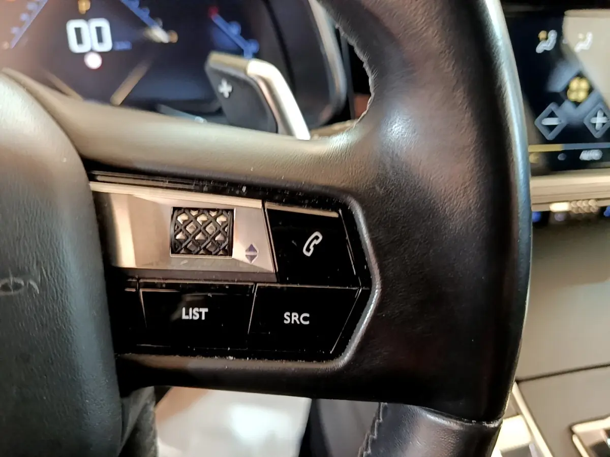 Gros plan sur le volant cuir noir du DS7 Crossback 2019, avec commandes intégrées et tableau de bord digital en arrière-plan.