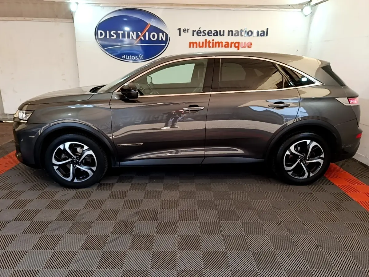 Vue de profil côté gauche d’un DS7 Crossback gris foncé avec toit clair, roues alliage et feux arrière LED visibles.