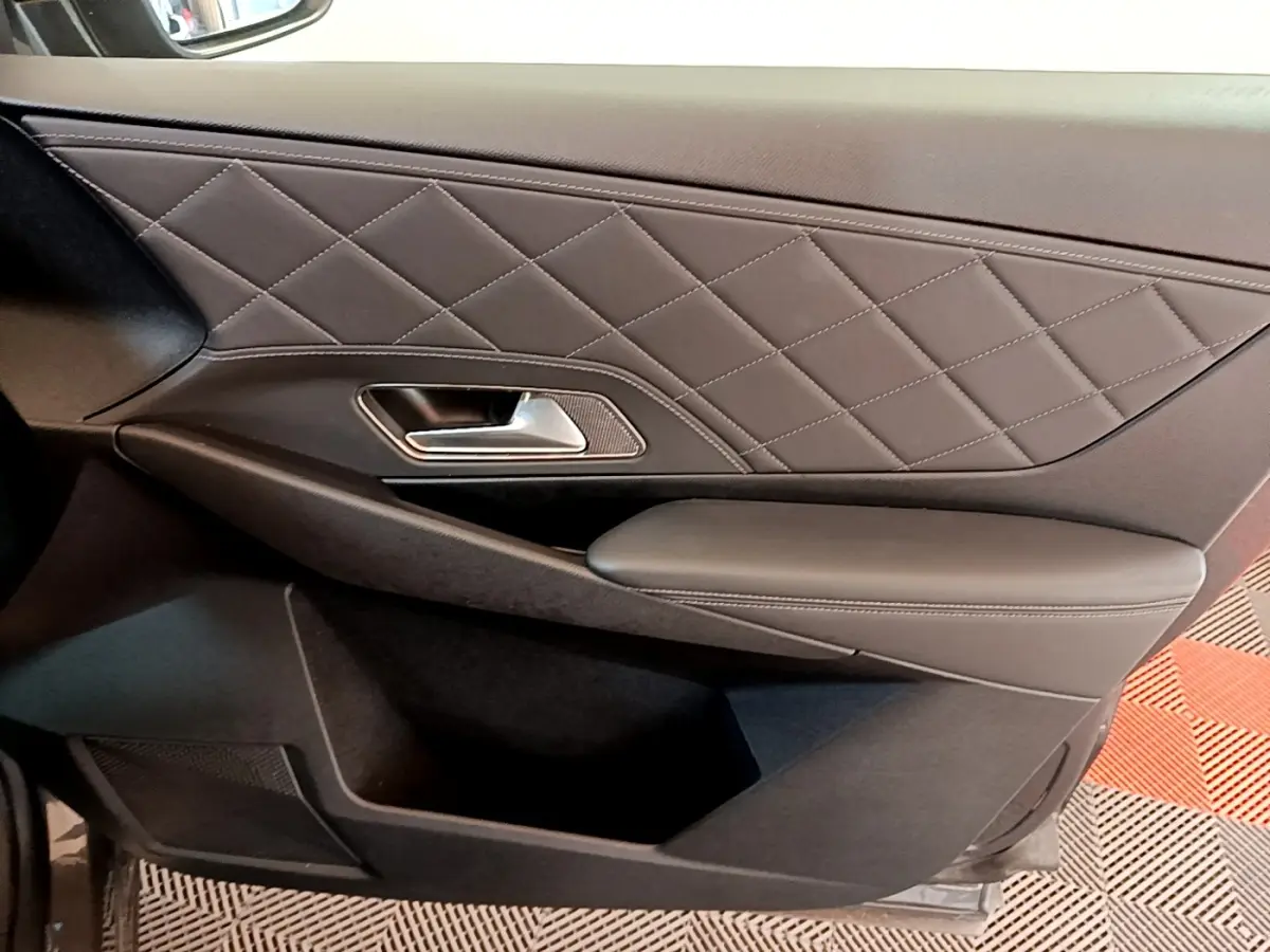 Gros plan sur la porte intérieure côté conducteur du DS7 Crossback gris foncé, avec surpiqûres en losange et poignée métal.