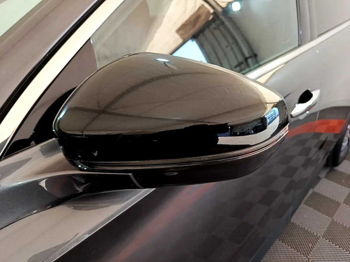 Gros plan sur le rétroviseur droit noir brillant du DS7 Crossback gris foncé, avec porte et poignée visibles en arrière-plan.