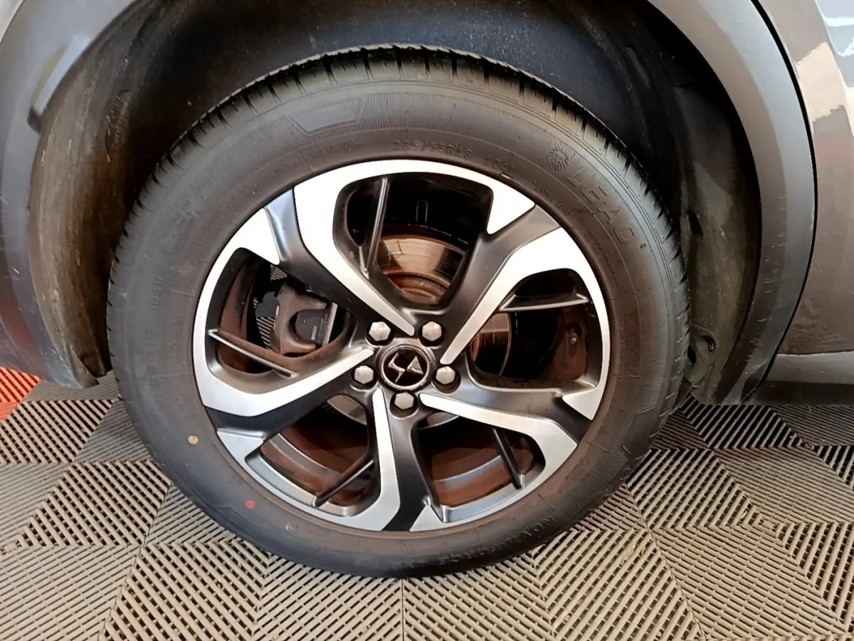 Gros plan sur la roue avant droite du DS7 Crossback gris foncé, mettant en valeur la jante alliage bicolore et le logo DS central.