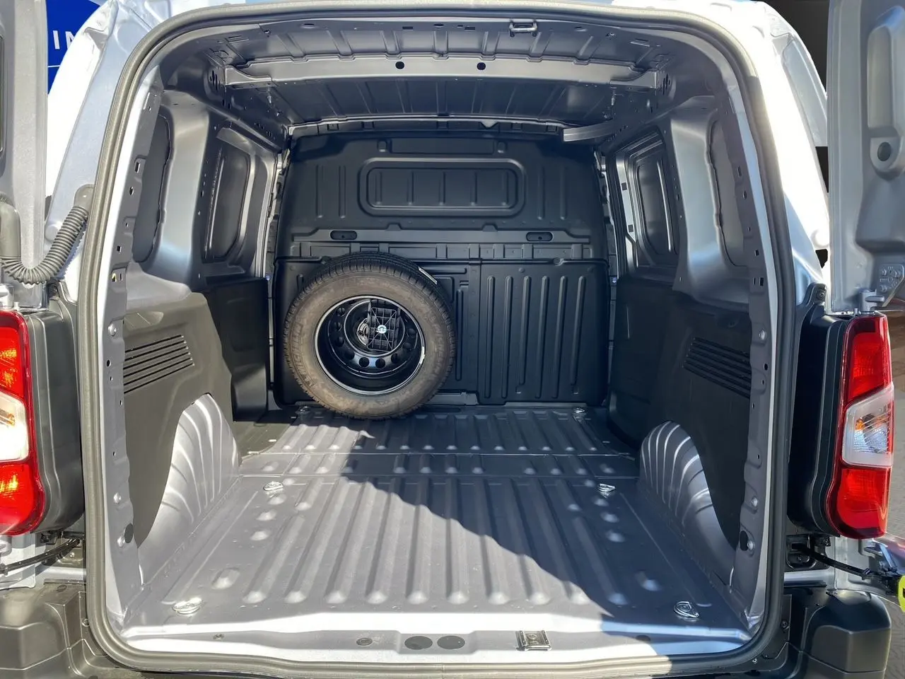 Vue arrière du Peugeot Partner Fourgon Dangel 4x4 gris Artense, montrant l'espace de chargement vide avec roue de secours fixée au fond.