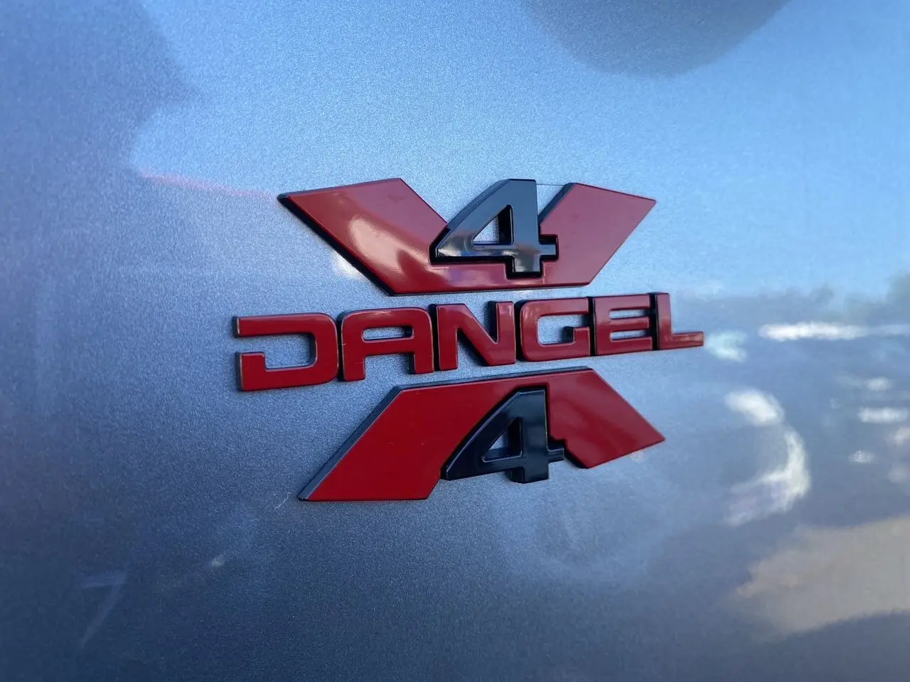 Gros plan sur l'écusson rouge Dangel 4x4 sur la carrosserie gris Artense métallisée du Peugeot Partner Fourgon 2025.