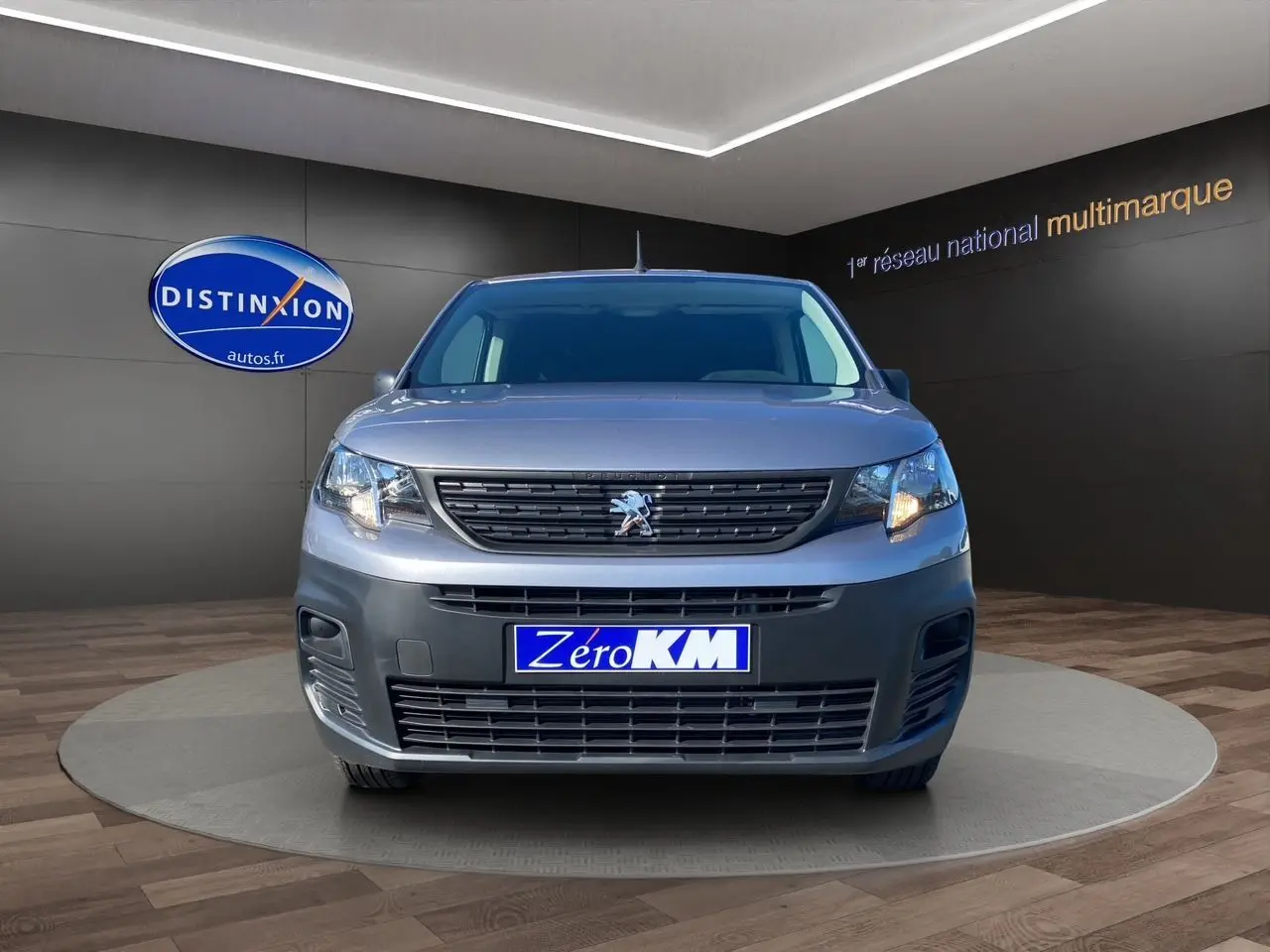 Vue frontale d'un Peugeot Partner Fourgon gris Artense métallisé avec calandre noire et plaque "Zéro KM" visible.