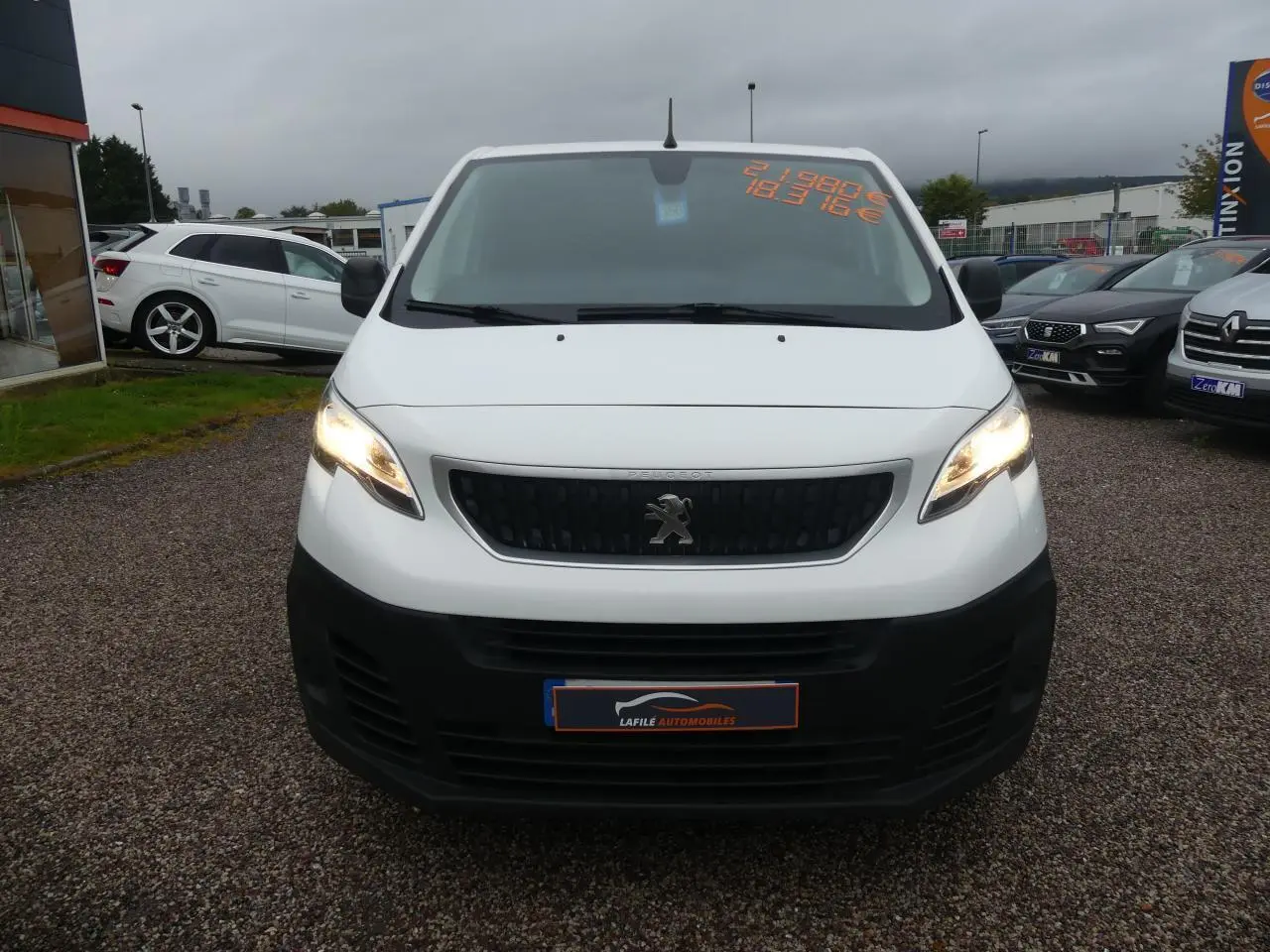 Vue frontale d'un Peugeot Expert Fourgon blanc avec calandre noire et phares allumés sur parking.