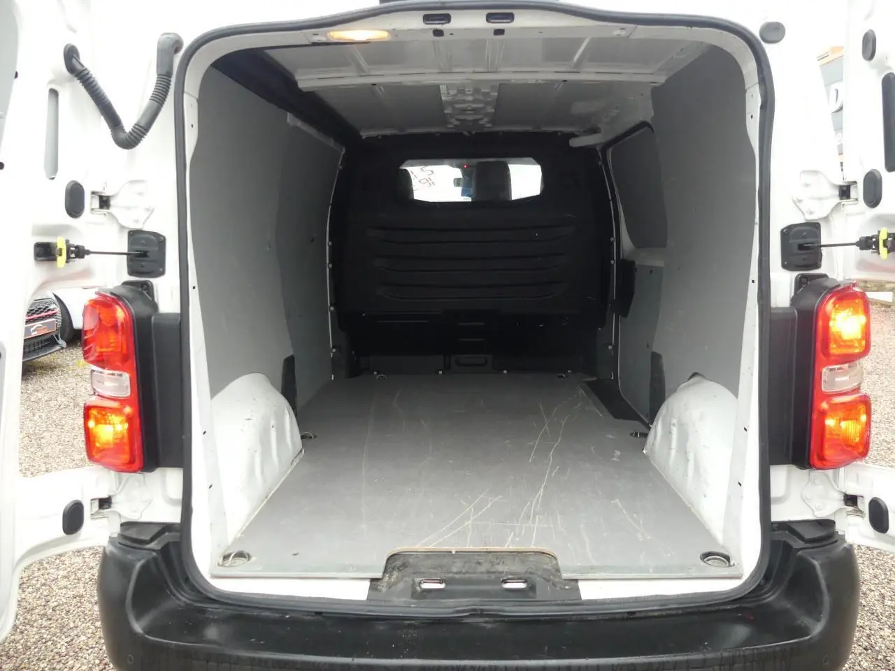 Vue arrière du Peugeot Expert Fourgon blanc 2019 avec portes ouvertes et plancher bois visible dans l’espace de chargement.