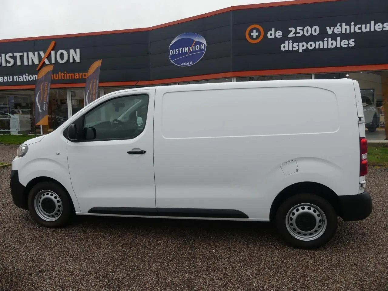 Vue de profil côté gauche d'un Peugeot Expert Fourgon blanc avec roues tôle et boucliers noirs sur parking.