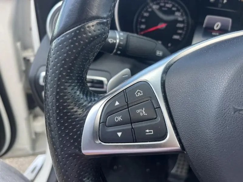 Gros plan sur le côté gauche du volant cuir perforé d’un Mercedes GLC Coupé blanc diamant avec commandes multifonctions.