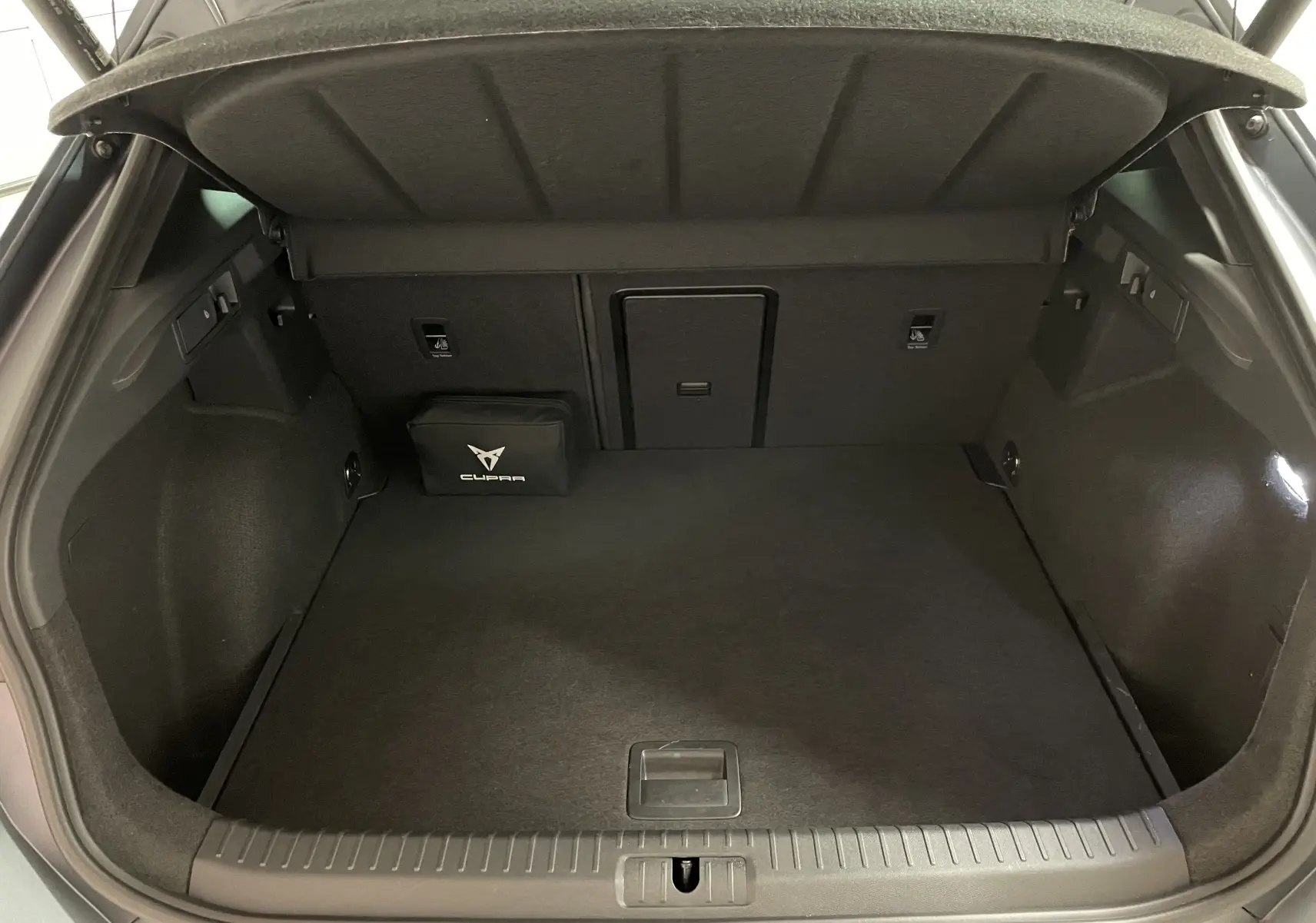 Coffre ouvert vu de l'arrière d'un CUPRA Formentor gris magnétique mat avec trappe de chargement et kit de secours marqué CUPRA.