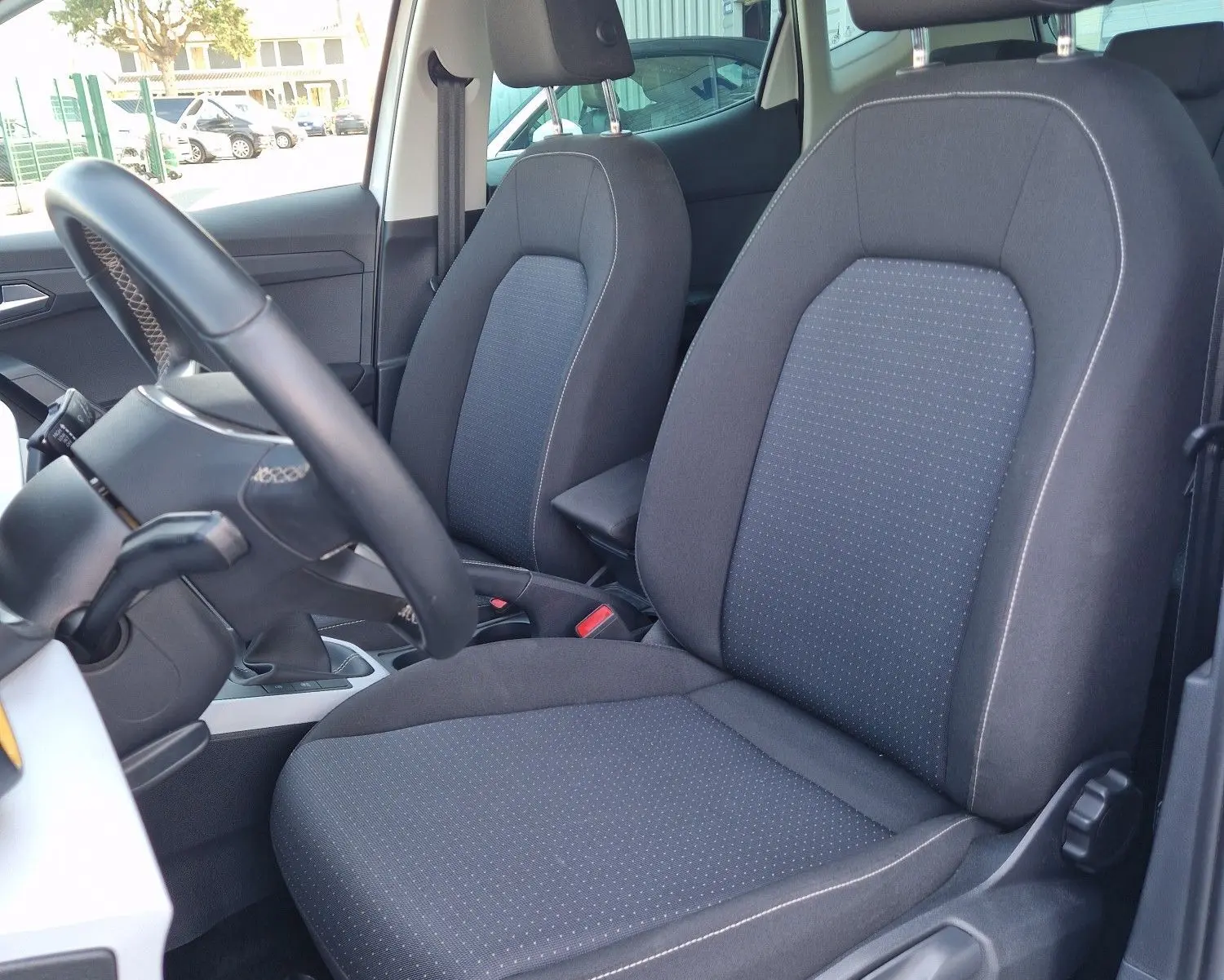 Vue intérieure côté conducteur du SEAT Arona 2025, sièges tissu noir avec surpiqûres, volant cuir multifonction visible.