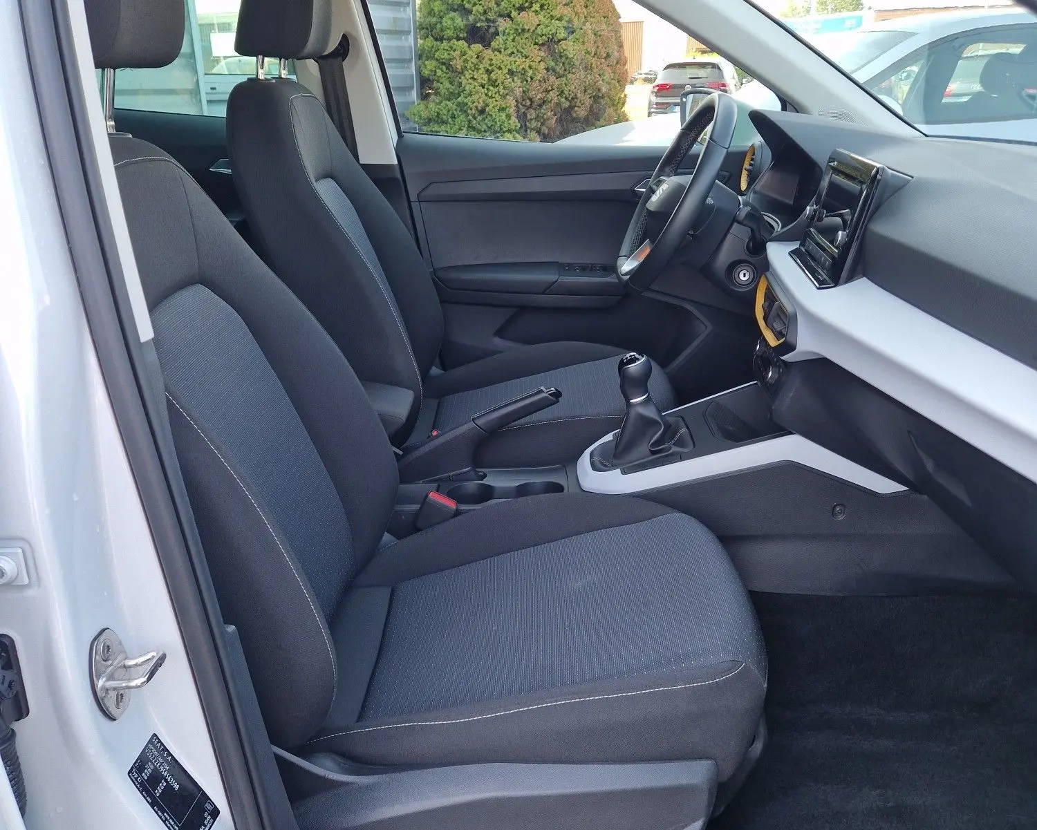 Intérieur côté conducteur du SEAT Arona blanc, montrant les sièges tissu noirs et la console centrale avec boîte manuelle.