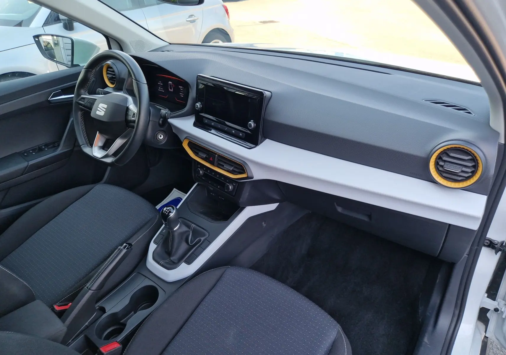 Vue intérieure côté conducteur de la SEAT Arona 2025, tableau de bord noir avec inserts jaunes et boîte manuelle.