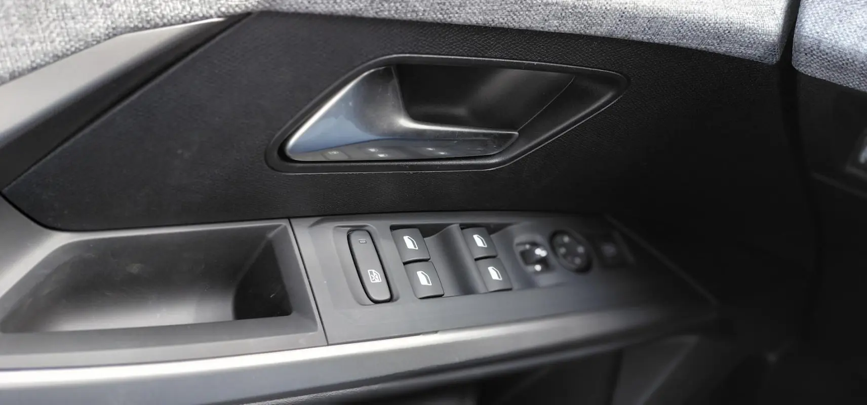 Gros plan sur la commande des vitres et la poignée intérieure côté gauche d’une Peugeot 3008 Hybrid noire, finition Allure.