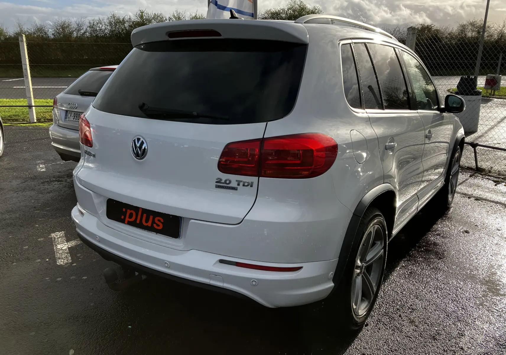 Volkswagen Tiguan blanc vu en 3/4 arrière droit avec badges 2.0 TDI et 4MOTION sur un parking humide.