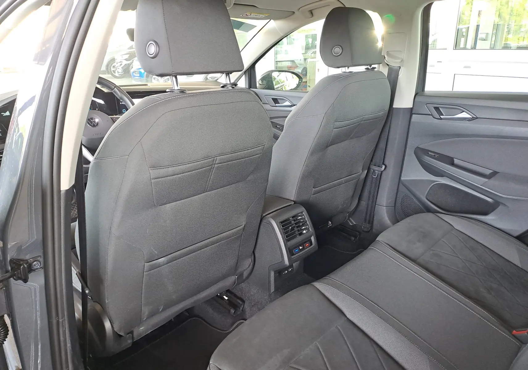 Vue intérieure arrière de la Volkswagen Golf VIII gris dauphin, montrant les sièges noirs et la console centrale avec aérateurs.