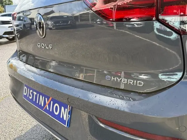 Gros plan sur l'arrière droit d'une Volkswagen Golf VIII gris dauphin avec badge e-Hybrid et plaque Distinxion.