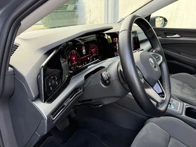Intérieur côté conducteur d'une Volkswagen Golf VIII gris dauphin, tableau de bord numérique et volant multifonction visible.
