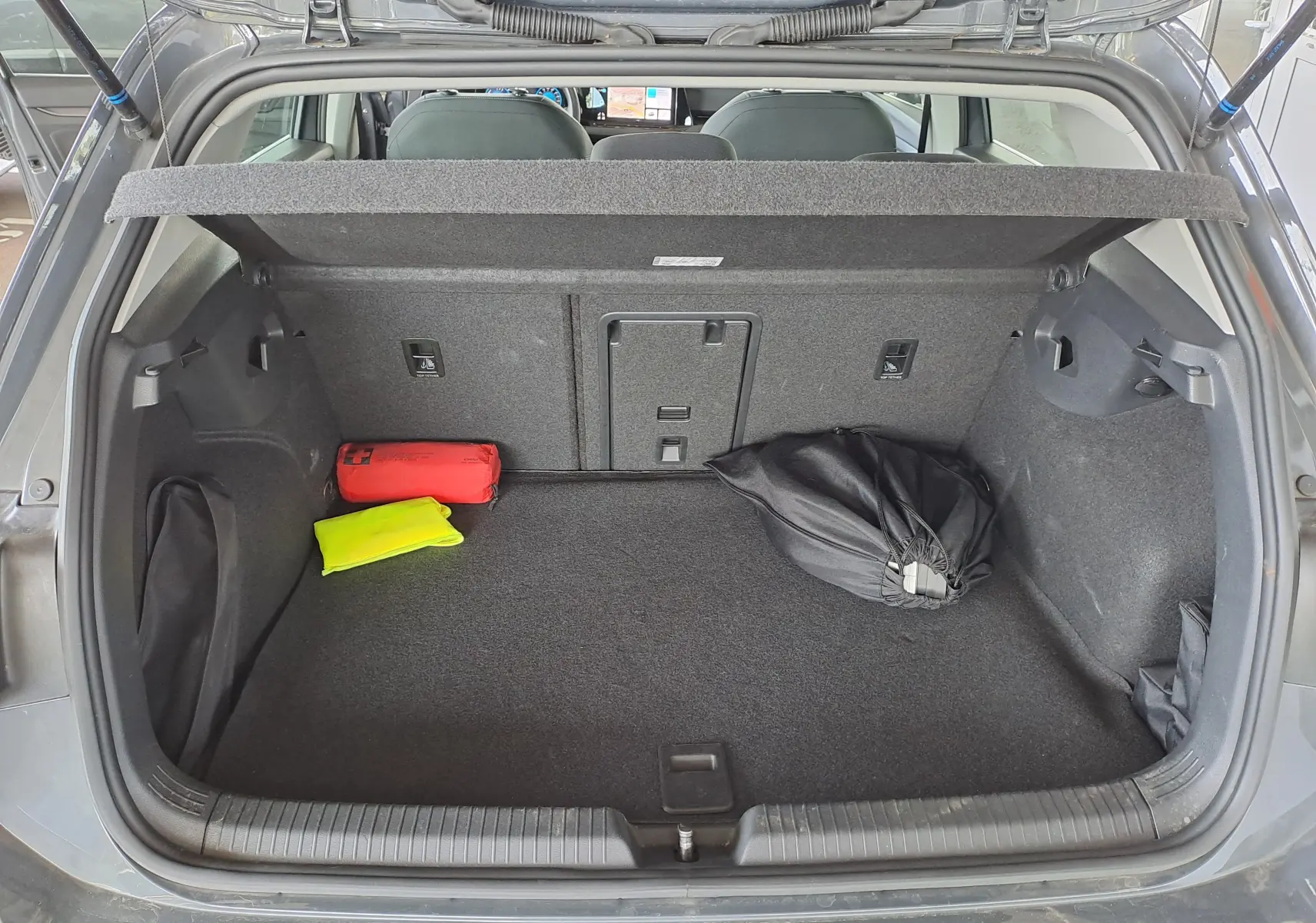 Coffre ouvert d'une Volkswagen Golf VIII gris dauphin, vue arrière montrant un kit de sécurité et un sac noir à l'intérieur.