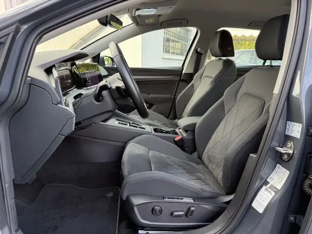 Vue intérieure côté conducteur de la Volkswagen Golf VIII gris dauphin, sièges avant en tissu gris avec réglages électriques.