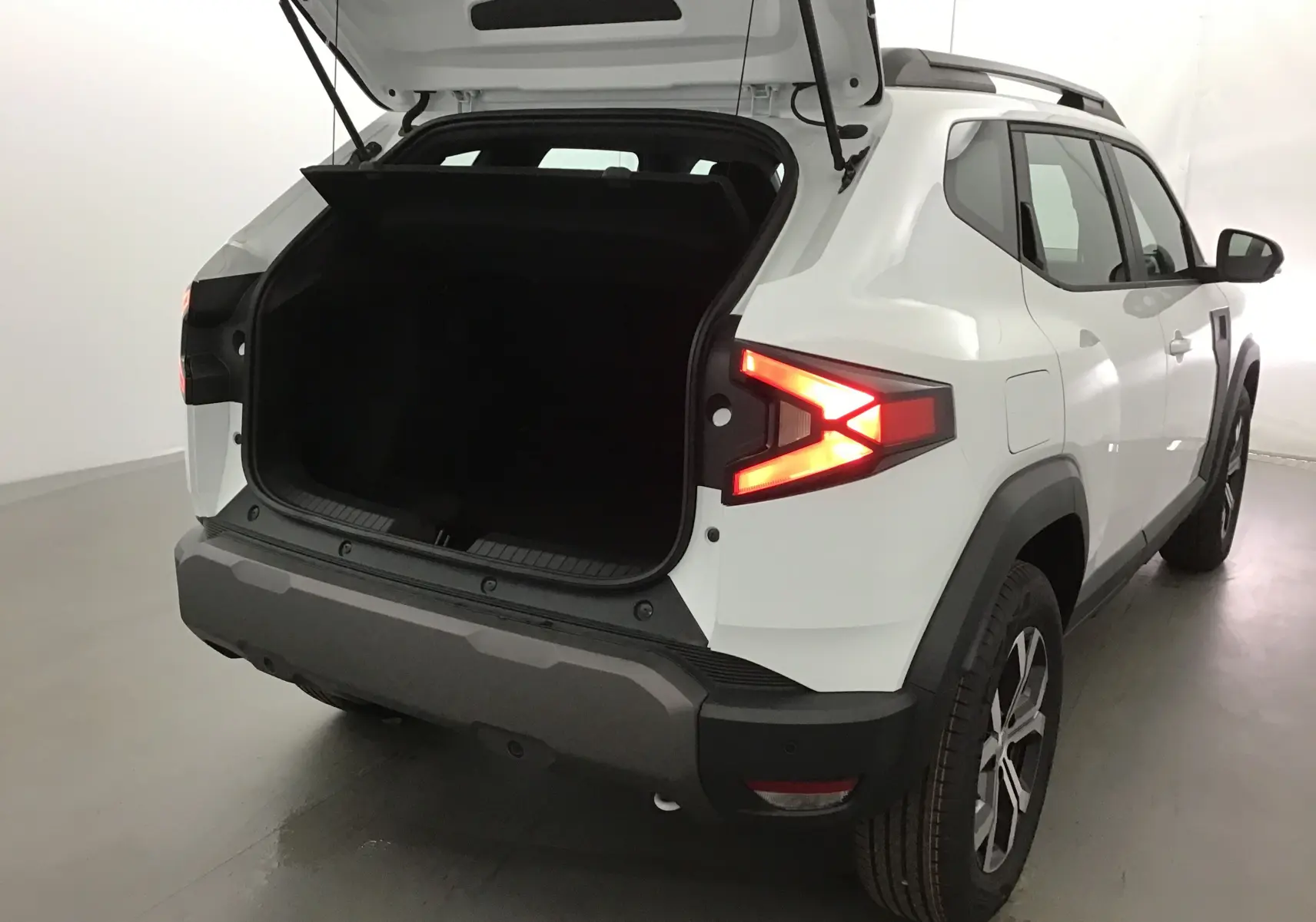 Vue arrière droite du Dacia Duster blanc glacier 2025 avec coffre ouvert et feux arrière allumés.