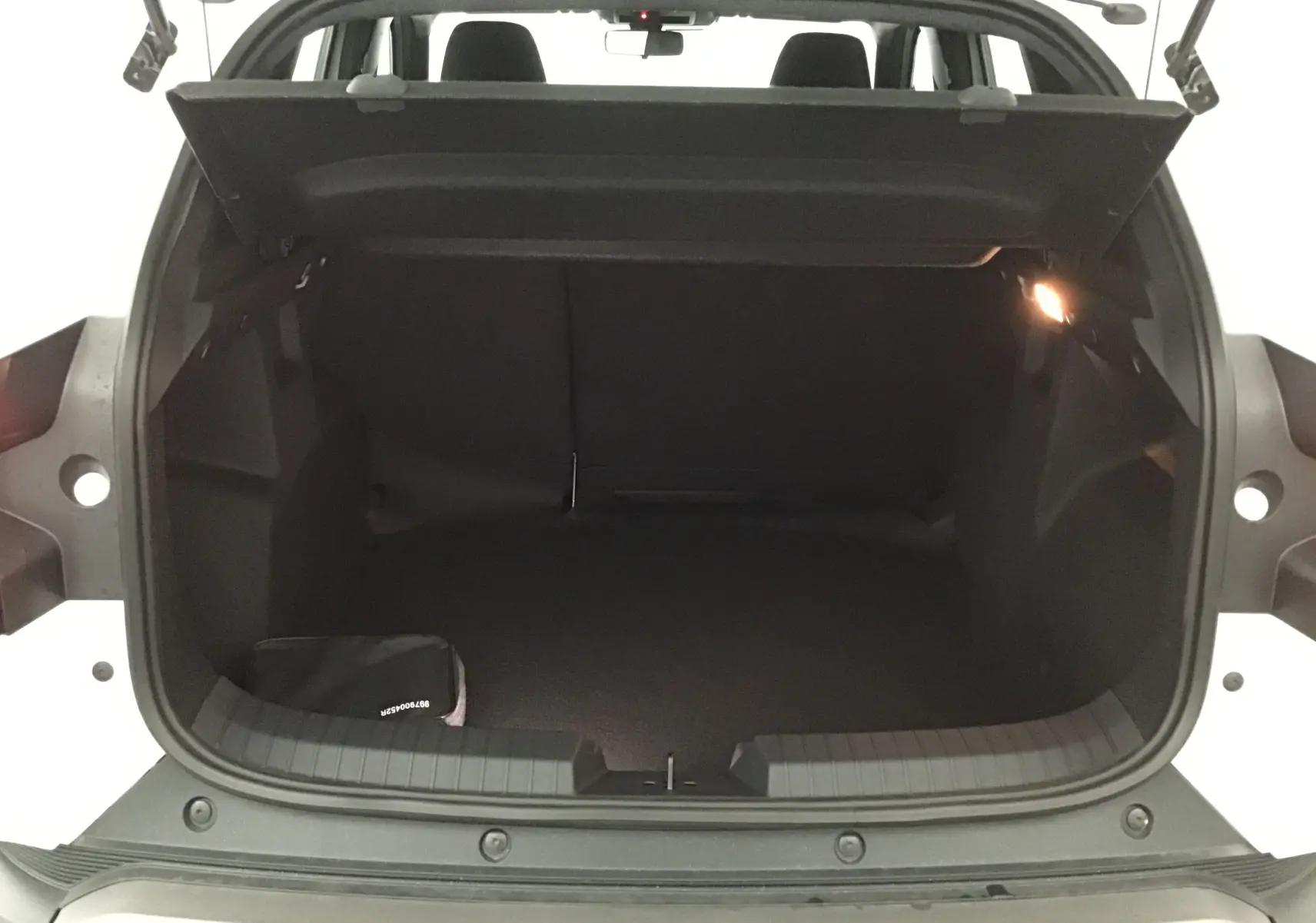 Coffre ouvert vu de l'arrière du Dacia Duster blanc glacier 2025, intérieur noir avec éclairage latéral allumé.