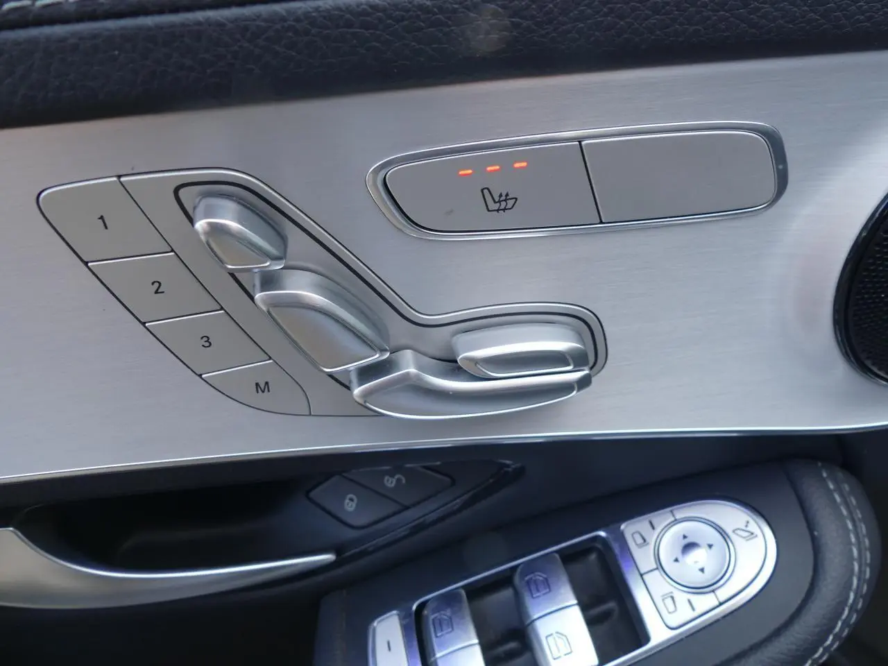 Gros plan sur les commandes de réglage de siège en aluminium brossé et cuir noir côté gauche d'une Mercedes GLC Coupé bleu foncé.