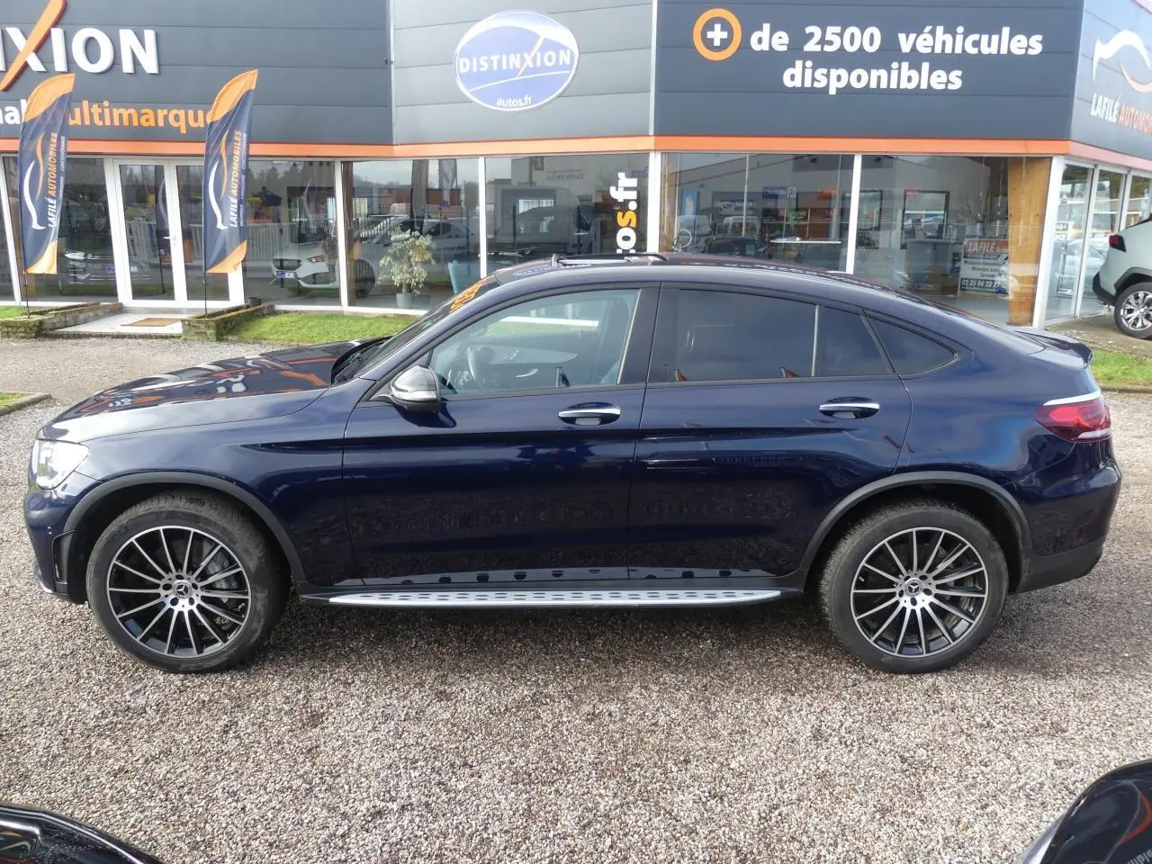Profil côté gauche d'un Mercedes GLC Coupé 300 hybride bleu foncé avec jantes AMG noires et marchepieds inox.