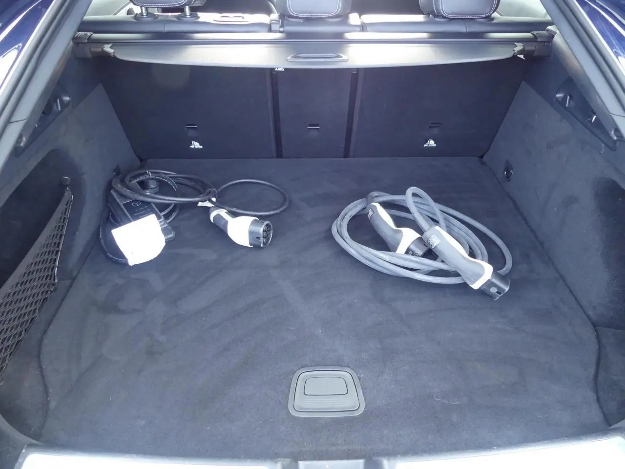 Coffre ouvert d’un Mercedes GLC Coupé hybride bleu foncé avec câbles de recharge sur tapis noir.