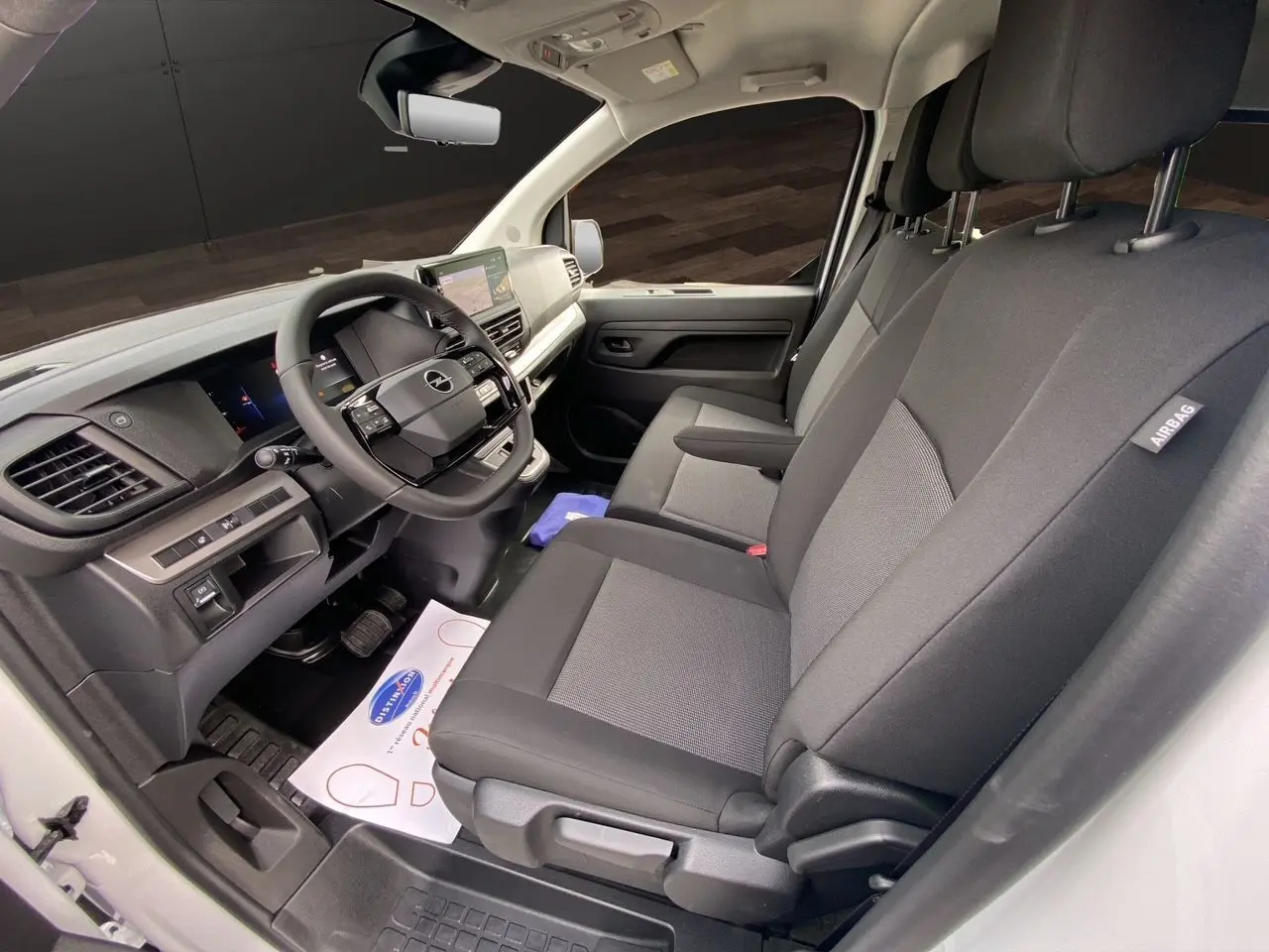 Vue intérieure côté conducteur de l'Opel Vivaro blanc 2025, montrant le tableau de bord et les sièges noirs en tissu.