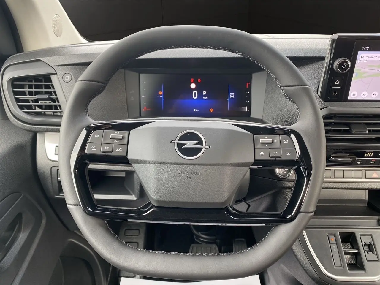 Volant noir de l'Opel Vivaro 2025 avec commandes intégrées et tableau de bord numérique visible en arrière-plan.