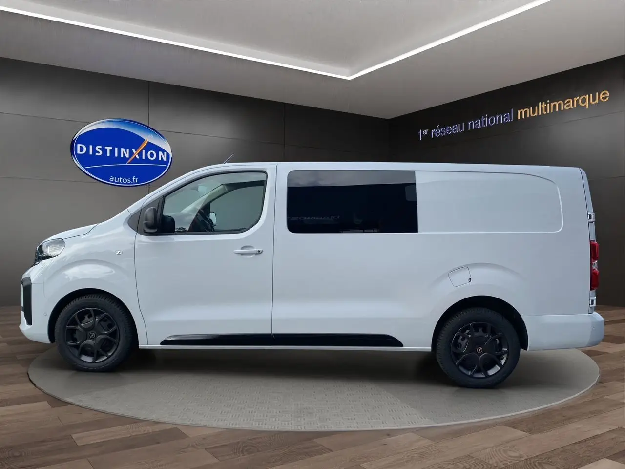Profil droit d'un Opel Vivaro blanc 2025 avec vitres teintées et jantes noires en intérieur showroom.