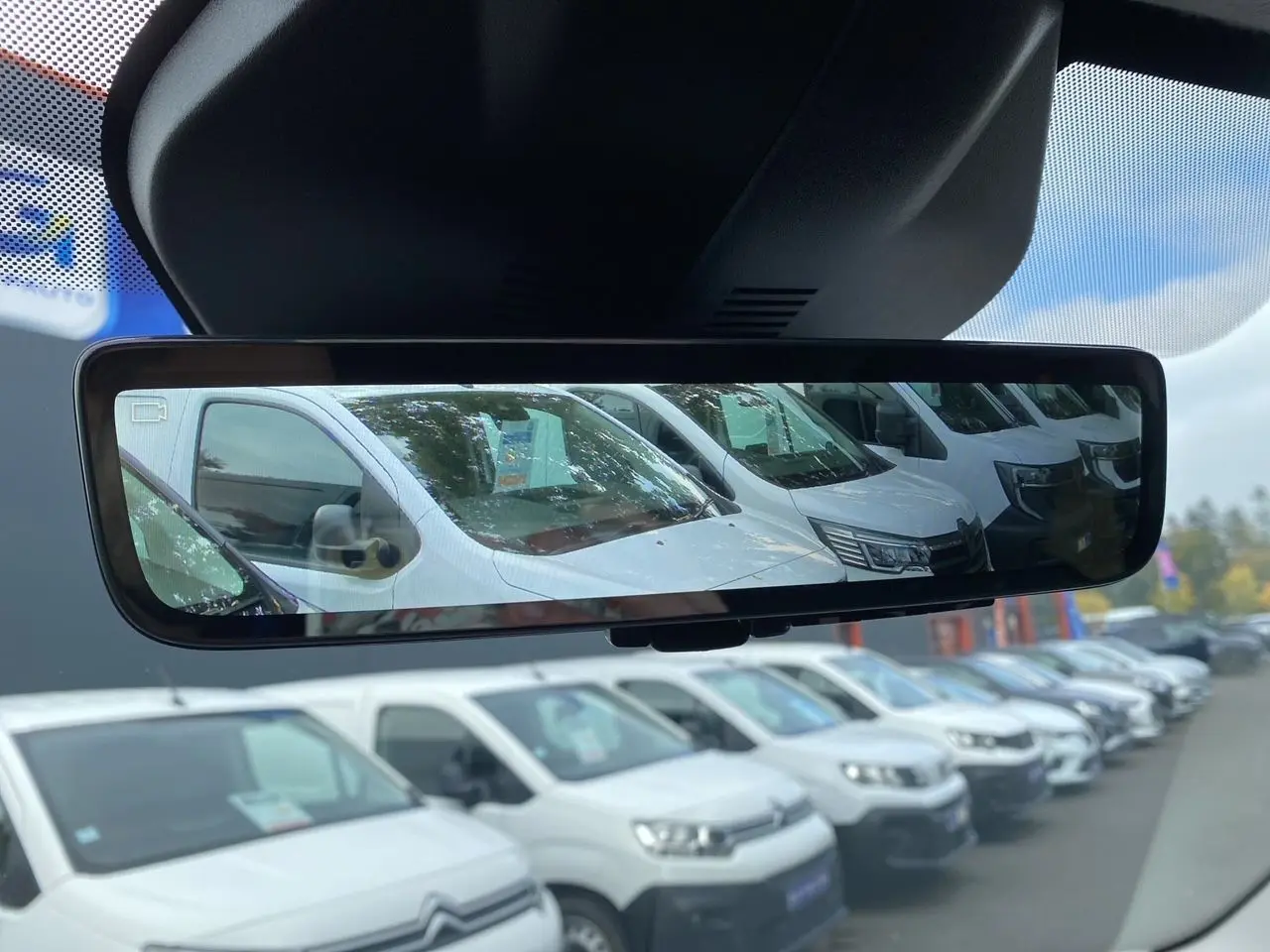 Rétroviseur intérieur montrant plusieurs fourgons blancs en stationnement, dont un Opel Vivaro blanc en 3/4 avant.