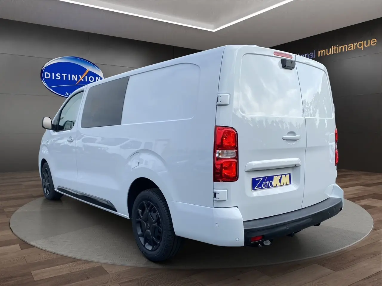 Vue 3/4 arrière droite d'un utilitaire Opel Vivaro blanc avec attelage et jantes noires en showroom.