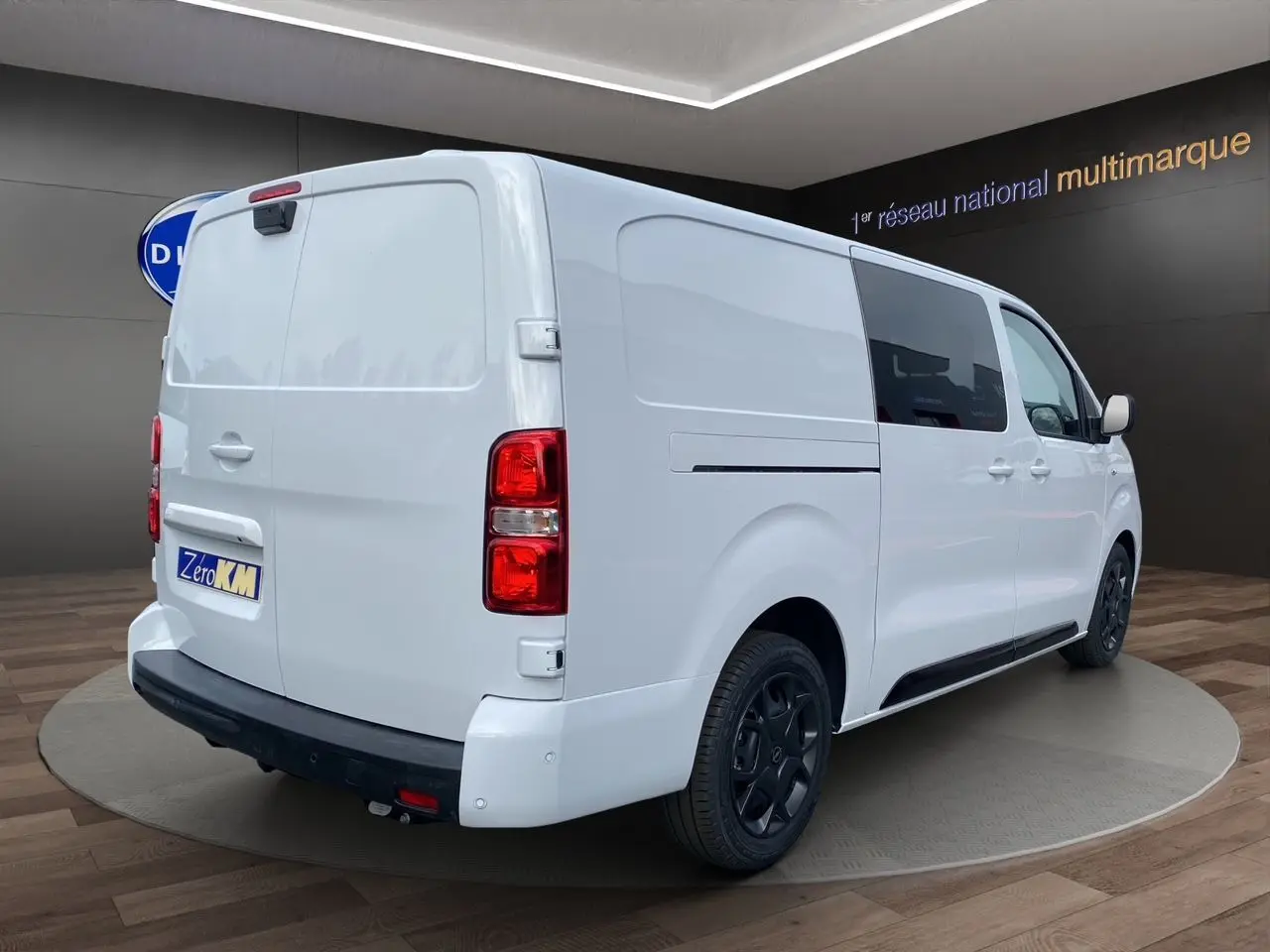 Vue 3/4 arrière droite d'un Opel Vivaro blanc avec jantes noires et attelage démontable en showroom.