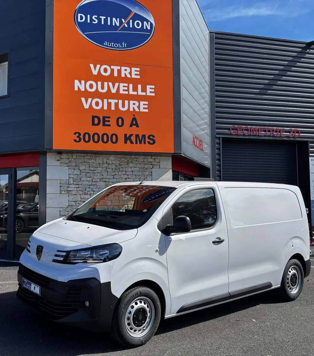 Peugeot Expert Fourgon blanc vu en 3/4 avant droit, stationné devant un bâtiment commercial avec panneau orange.