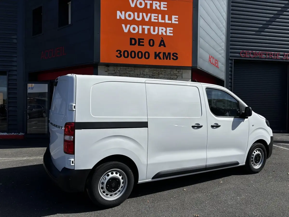 Peugeot Expert Fourgon blanc vu de profil côté droit, stationné devant un bâtiment commercial.