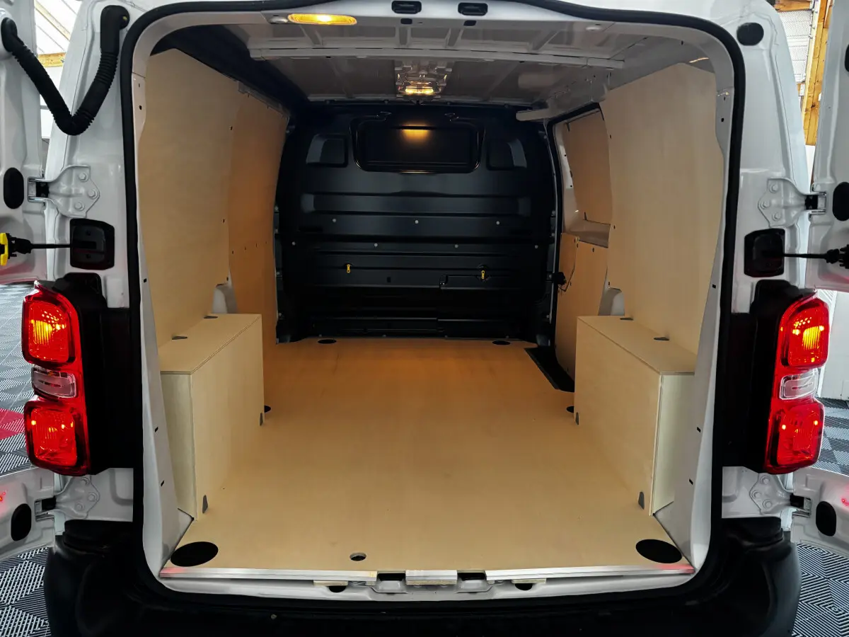 Vue arrière du Peugeot Expert Fourgon blanc 2025 avec intérieur de chargement en bois clair et éclairage intérieur allumé.