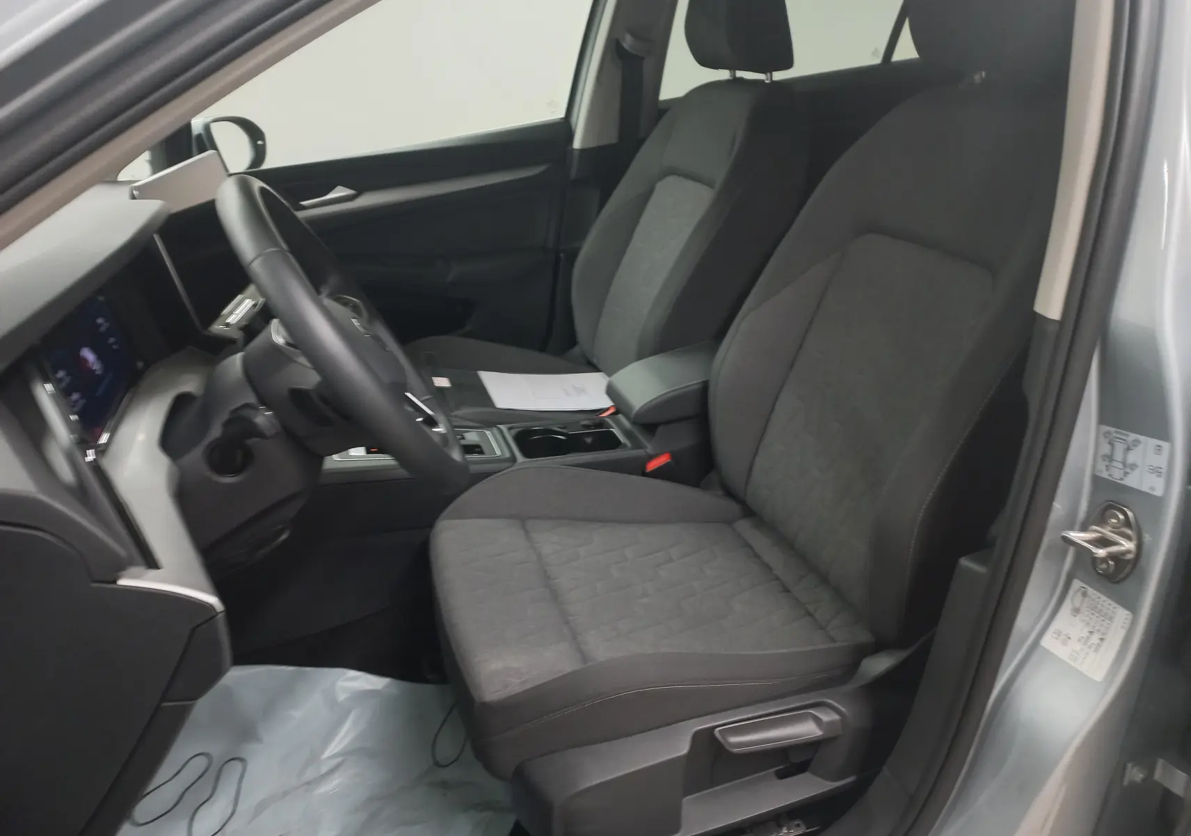 Vue intérieure côté conducteur de la Volkswagen Golf 1.5 eHybrid 2025 en Argent Dolomite, sièges tissu gris et tableau de bord moderne.